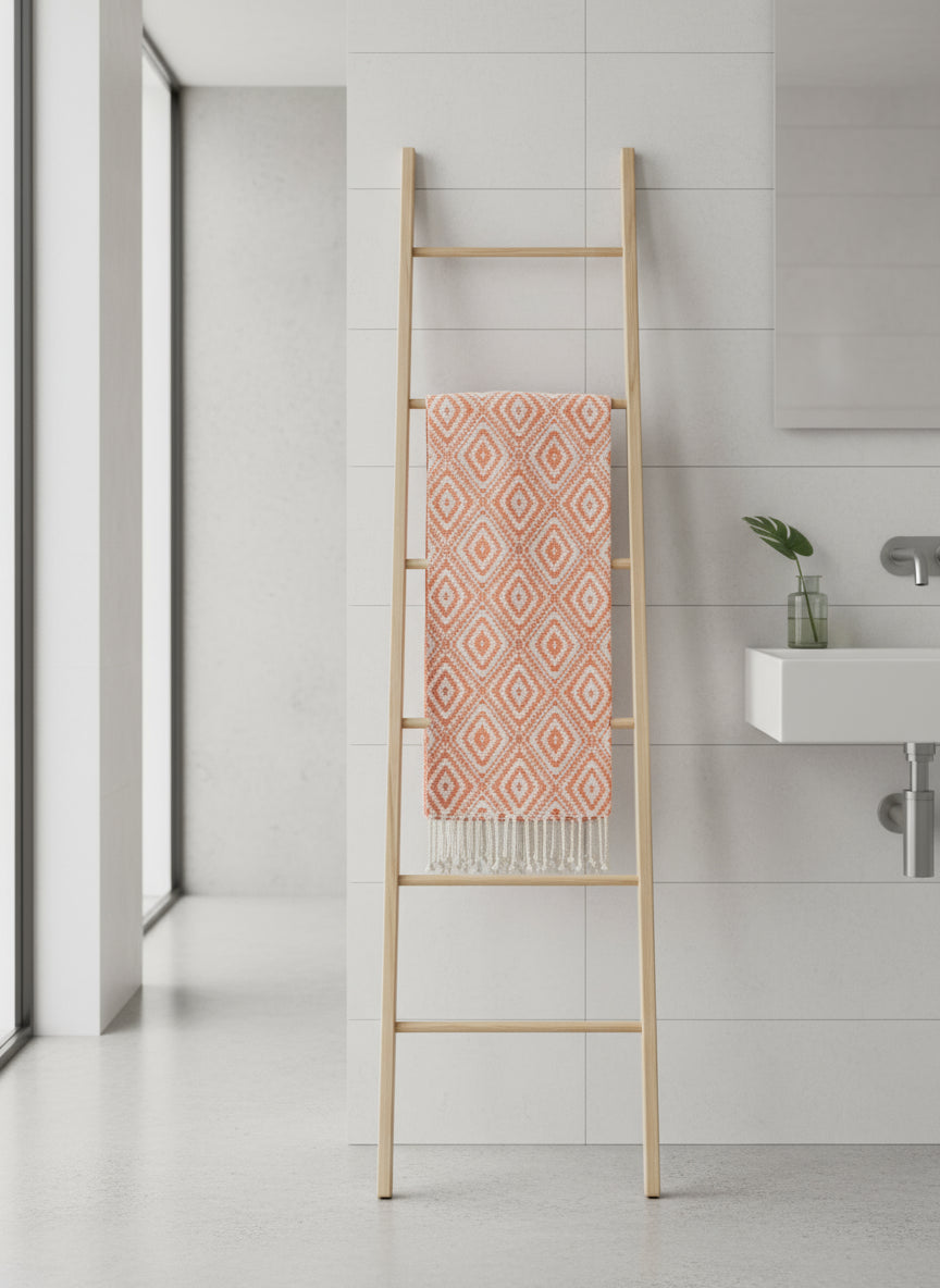Bathroom with a wooden towel ladder holding a pink patterned Fouta towel against a tiled wall.