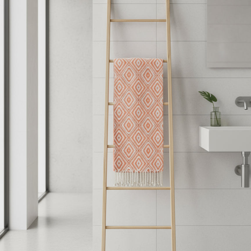 Bathroom with a wooden towel ladder holding a pink patterned Fouta towel against a tiled wall.