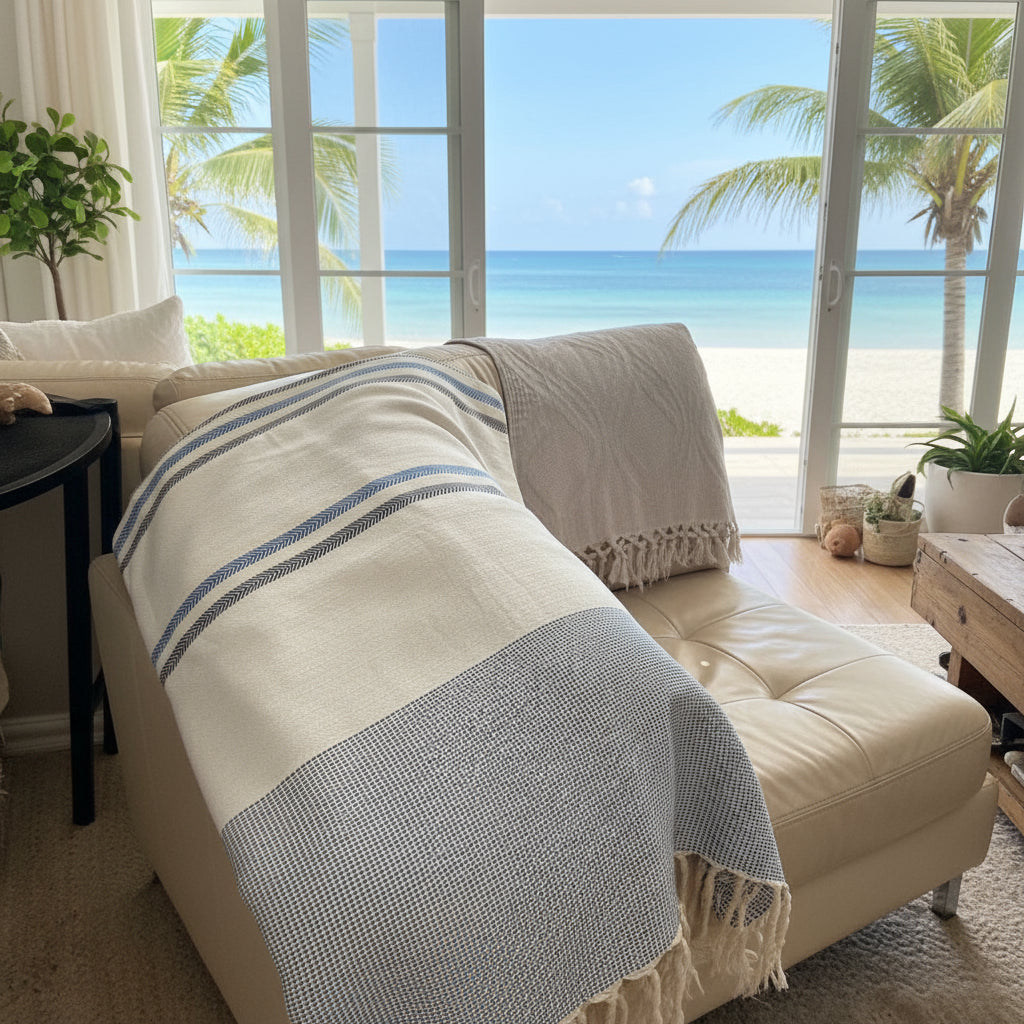 Beige sofa with a striped XL Fouta towel in a room with large windows showing a beach view.