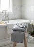 Blue Natte Fouta bathrobe on a stool next to a white bathtub in a bathroom.