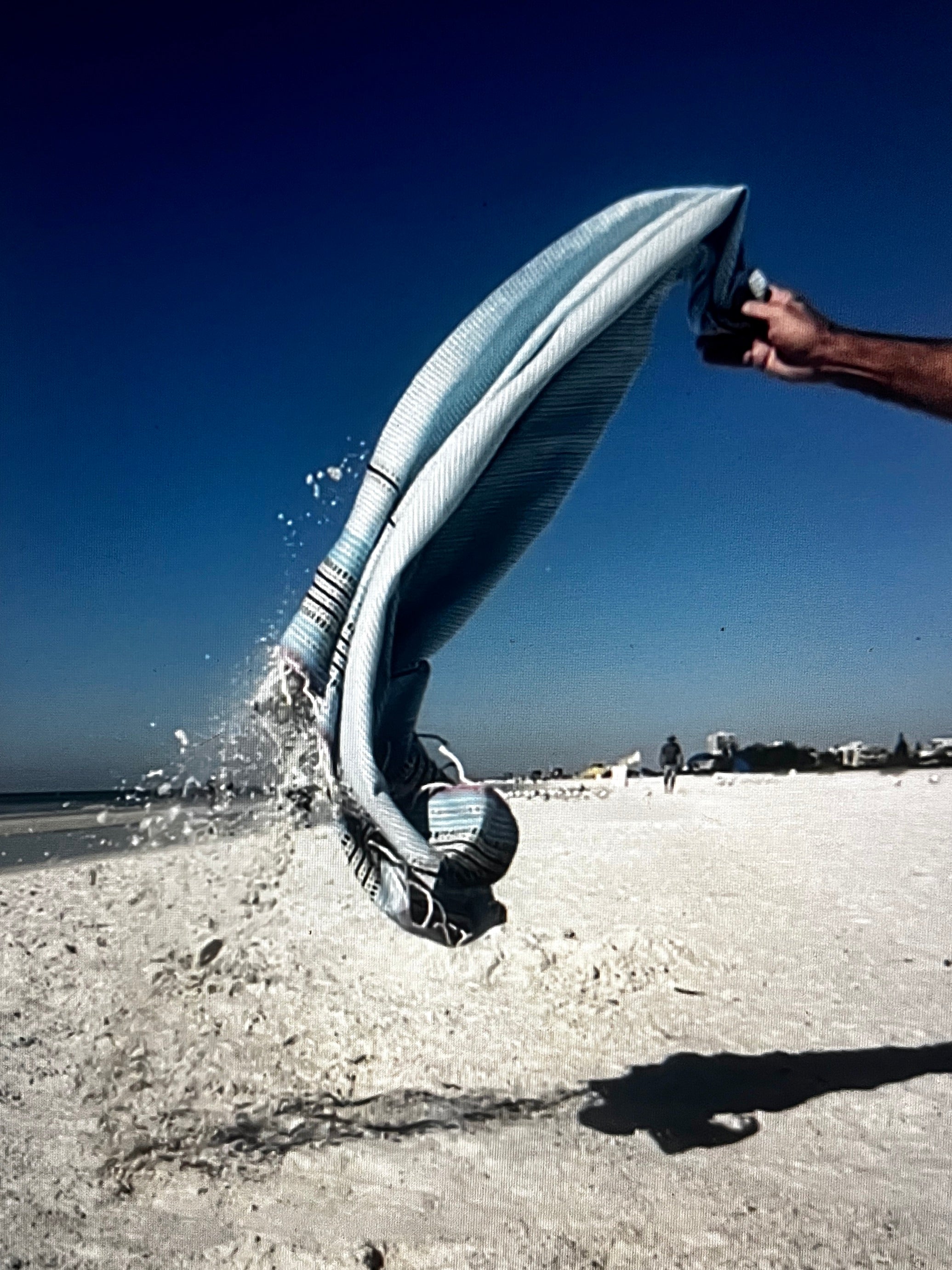 an arm pulling a fouta towel off a beach, spraying sand in the process